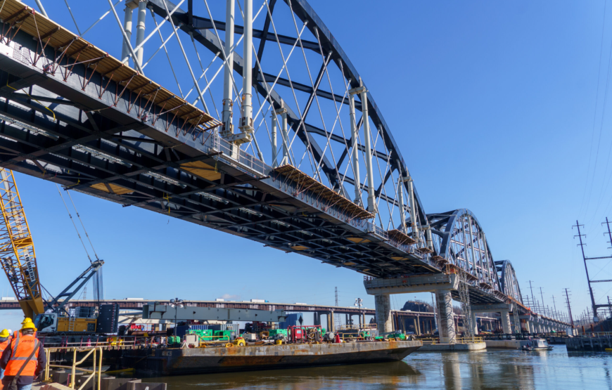 Steel arch spans of the new Portal North Bridge over the Hackensack River with a crane and work barge below
